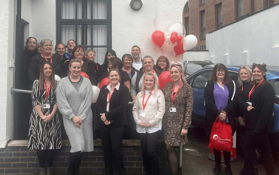 Group of people standing in front of a white church building, celebrating a rebrand event with red and white balloons in the background.