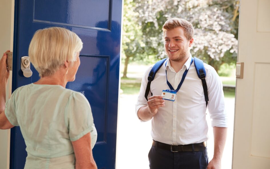 A woman answering a door to a man wearing a back pack, showing his badge. Home Care vs Care Homes
