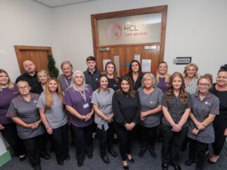 Image of a group of people in an office setting, wearing a care assistant uniform, stood in front of an office building.