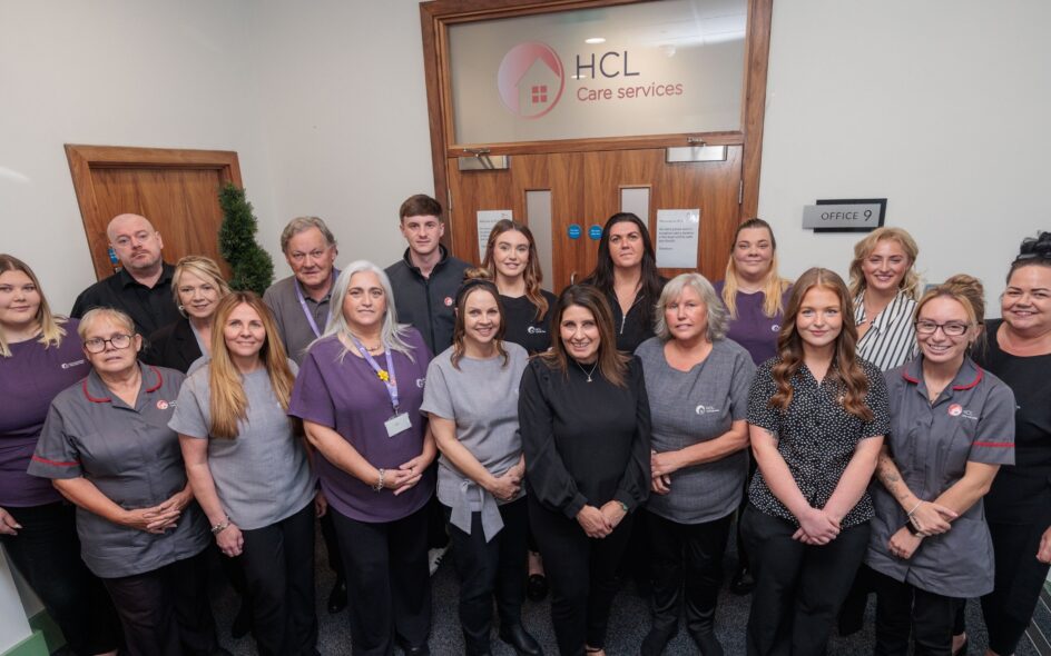 Image of a group of people in an office setting, wearing a care assistant uniform, stood in front of an office building.