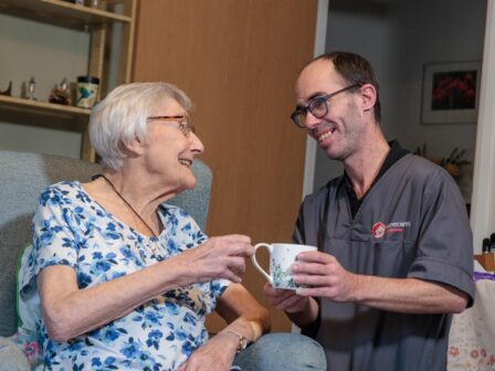 Image of a service user and a Care Assistant, smiling and laughing whilst holding a cup of tea.