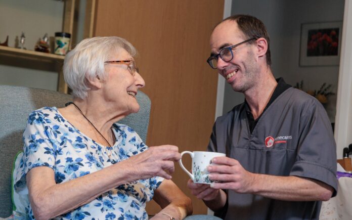 Image of a service user and a Care Assistant, smiling and laughing whilst holding a cup of tea.