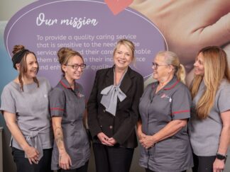 An image of 5 people in an office setting, smiling and laughing.