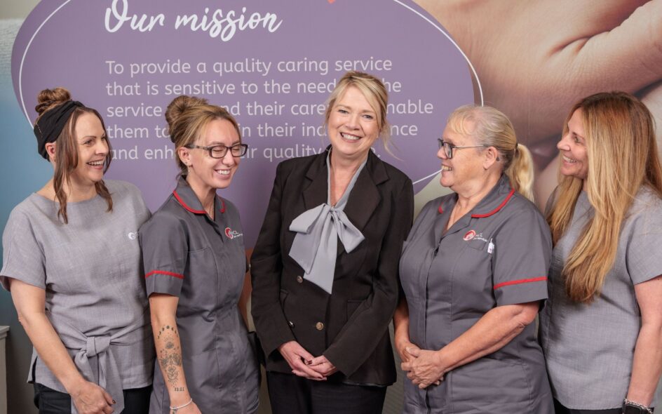 An image of 5 people in an office setting, smiling and laughing.