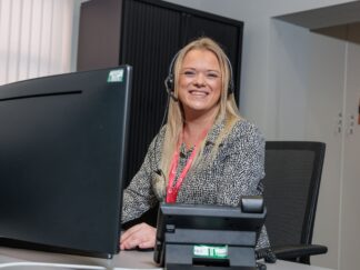 Image of a woman on the phone, sat at her desk wearing a headset.