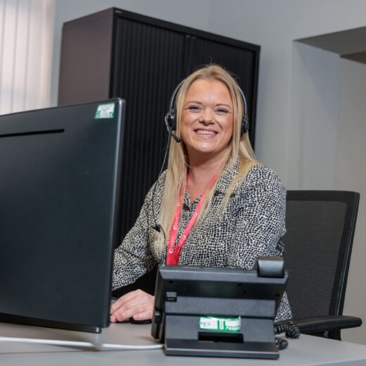 Image of a woman on the phone, sat at her desk wearing a headset.