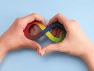 Image of a pair of hands in the shape of a love heart, holding a rainbow coloured infinity sign against a blue background.