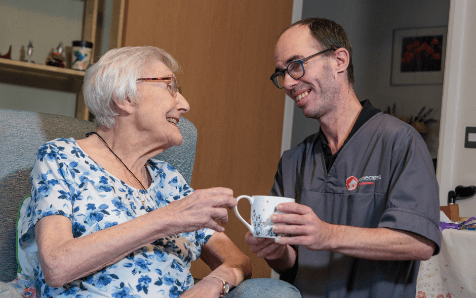 An image of a Care Assistant and an elderly lady, bonding over a cup if tea.