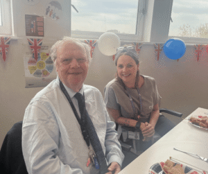 An image of a man and a woman sat at an afternoon tea party, smiling for the camera.