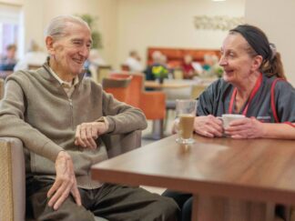 Image of two people sat at a table in a canteen setting, chatting over a cup of tea, highlighting companionship services.