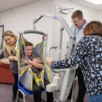 Image of a group of individuals in a learning environment, practicing using a hoist.