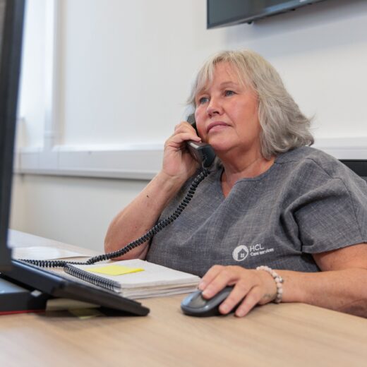 An image of a woman in a grey uniform, sat at a desk answering a phone call.