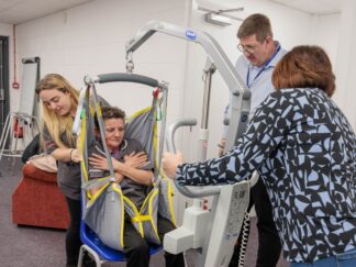 Image of a group of individuals in a learning environment, practicing using a hoist.