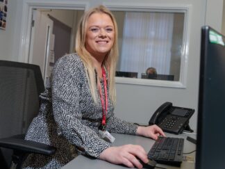 An image of a woman sat at a desk answering a phone call.