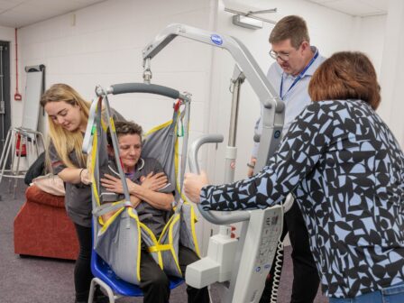 Image of a group of individuals in a learning environment, practicing using a hoist.