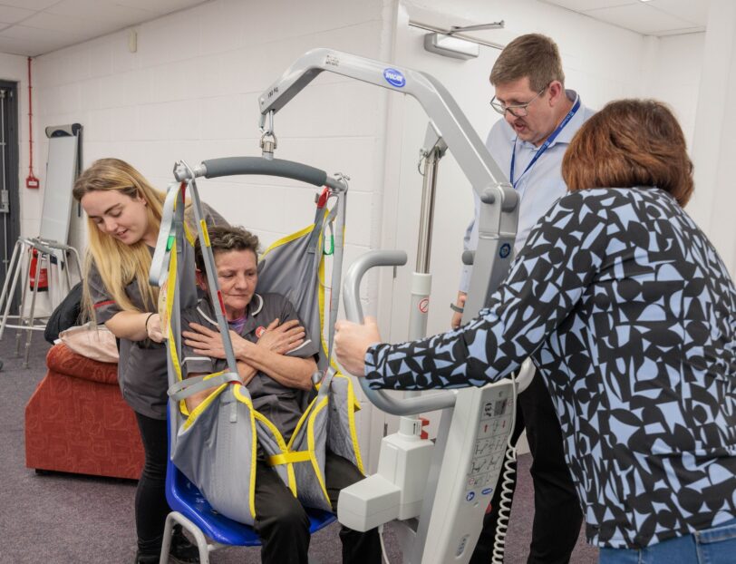 Image of a group of individuals in a learning environment, practicing using a hoist.