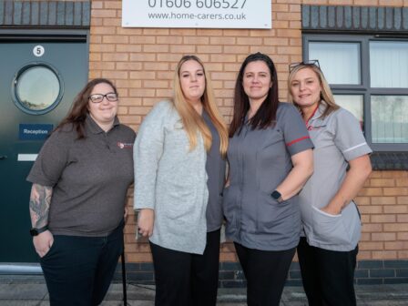 4 people in a care assistant uniform, stood in front of a brick building.