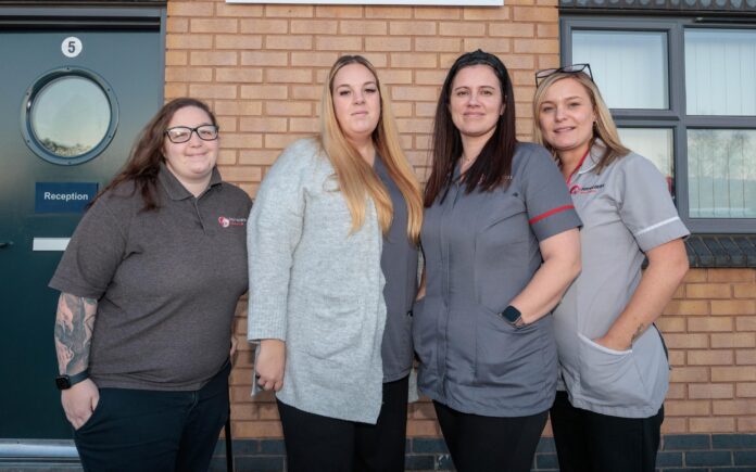 4 people in a care assistant uniform, stood in front of a brick building.