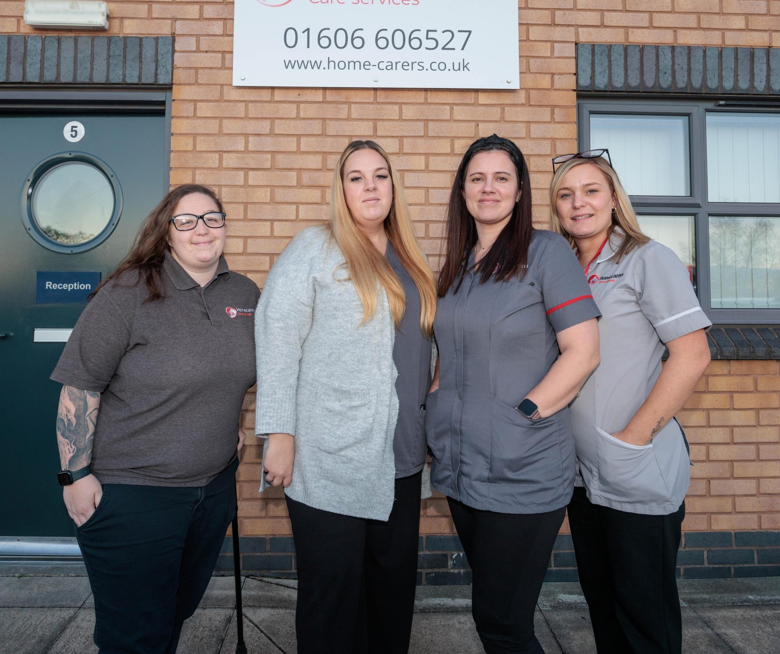 4 people in a care assistant uniform, stood in front of a brick building.