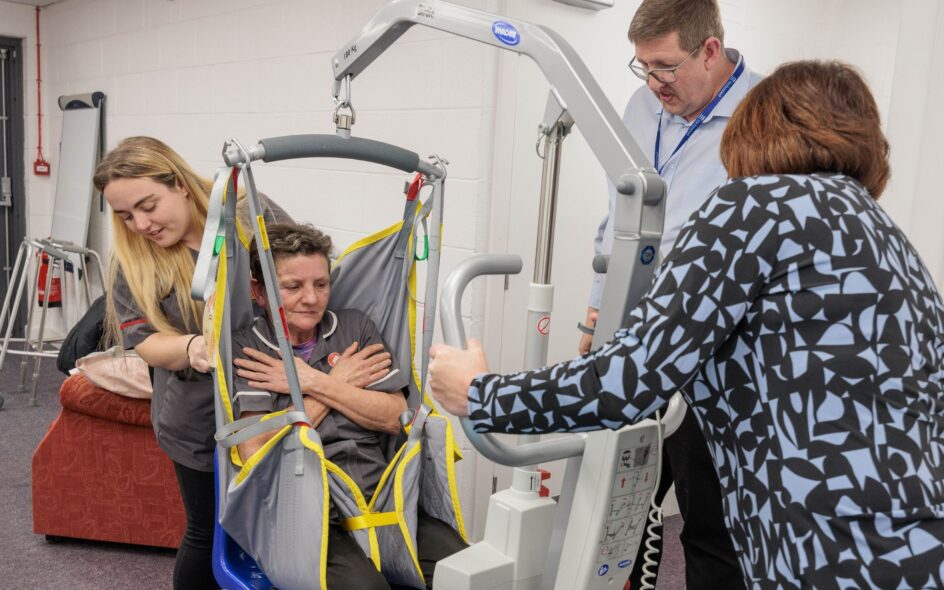 Image of a group of individuals in a learning environment, practicing using a hoist.