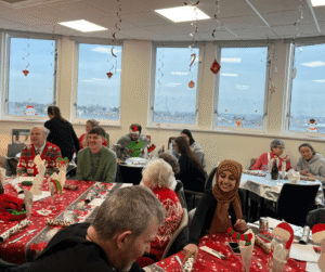 Image of people in an office setting, sitting at tables and laughing whilst enjoying a Christmas party.