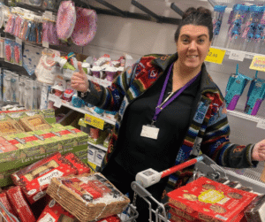 Image of a happy, smiling person in a supermarket, with a trolley full of goods.