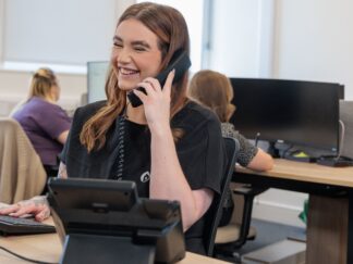 An image of a woman in an office environment sat at a desk, answering a phone call.