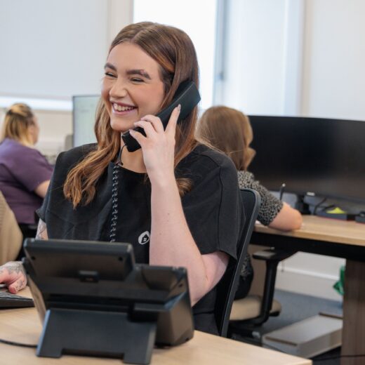 An image of a woman sat at a desk, answering a phone call.