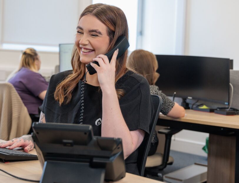 An image of a woman sat at a desk, answering a phone call.