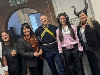 A group of individuals in an office setting, taking part in a Halloween costume competition.