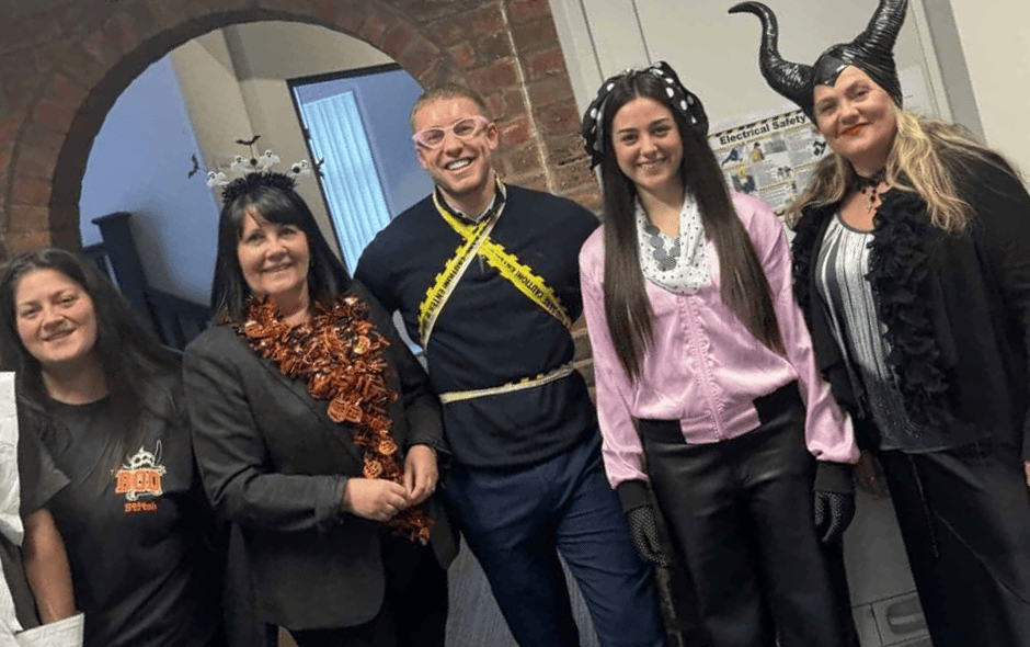 A group of individuals in an office setting, taking part in a Halloween costume competition.