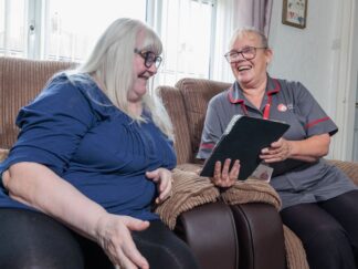 An image of one service user and a Care Assistant on a couch, smiling and laughing with each other.