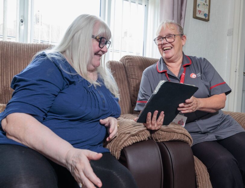 An image of one service user and a Care Assistant on a couch, smiling and laughing with each other.