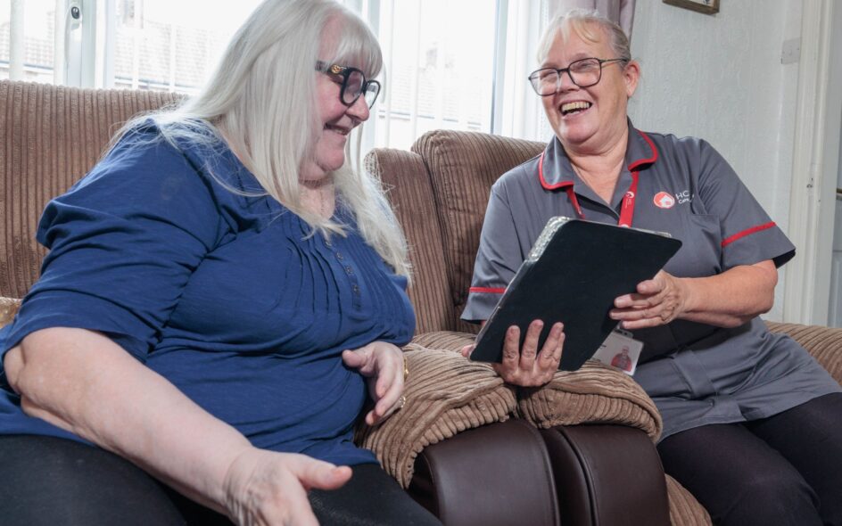 An image of one service user and a Care Assistant on a couch, smiling and laughing with each other.