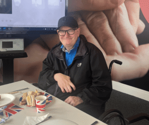 An image of a man sat at an afternoon tea party, smiling for the camera.