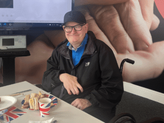 An image of a man sat at an afternoon tea party, smiling for the camera.