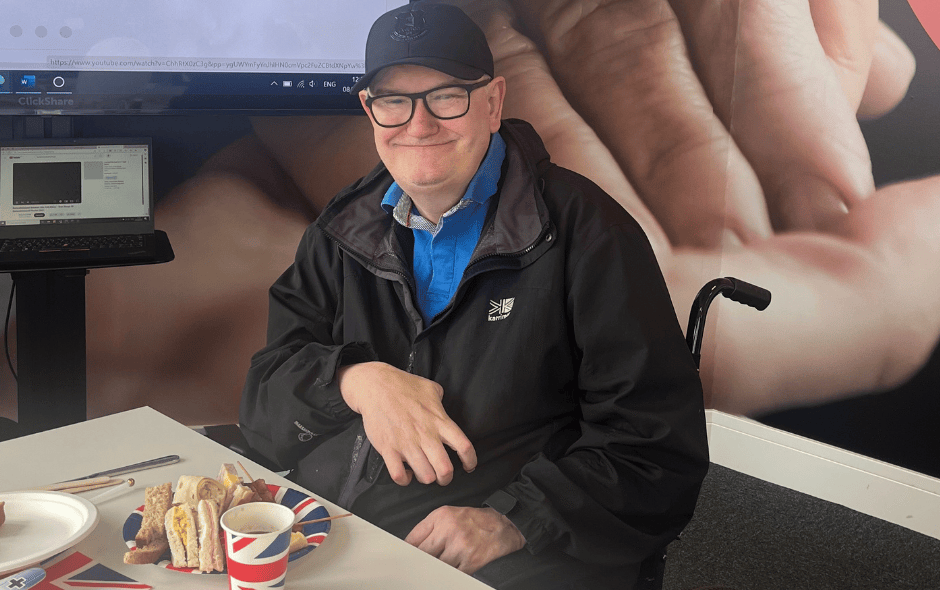 An image of a man sat at an afternoon tea party, smiling for the camera.