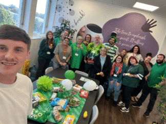 A group of individuals all wearing green for a fundraiser, standing behind a green table full of buffet food.