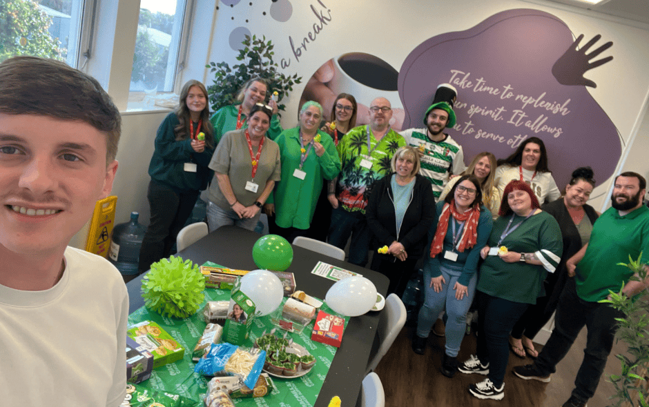 A group of individuals all wearing green for a fundraiser, standing behind a green table full of buffet food.