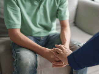 Image of two people holding hands, whilst one sits down on a beige couch.