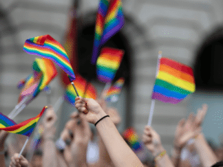 Image of a crowd waving rainbow coloured flags.
