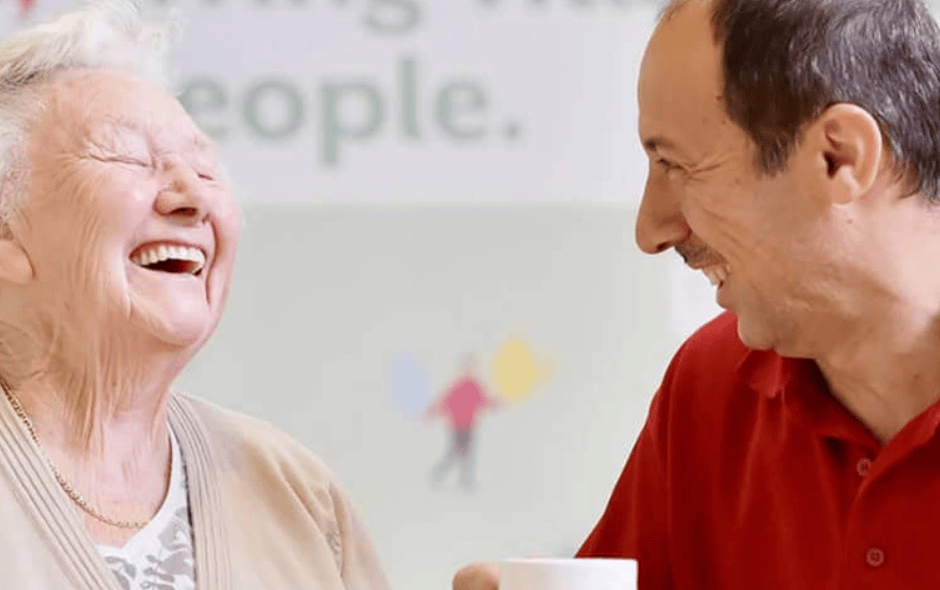 An image of 2 people laughing over a cup of tea.