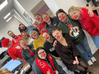 A group of people in an office setting, wearing red noses for a fundraiser.