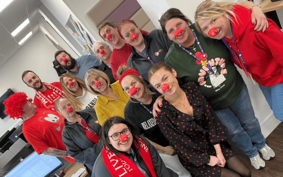 A group of people in an office setting, wearing red noses for a fundraiser.
