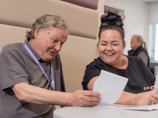 An image of a man and a woman sat at a table, smiling at a piece of paper.