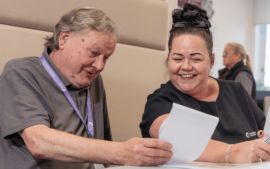 An image of a man and a woman sat at a table, smiling at a piece of paper.