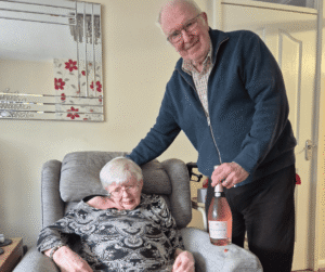 An image of a couple holding a bottle of prosecco and smiling for the camera.