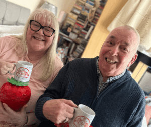 An image of a couple holding mugs and smiling for the camera.
