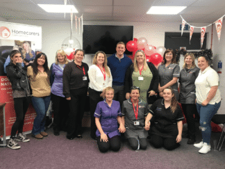 Image of a room full of colleagues, taking part in celebrations with red balloons and red bunting in the background.