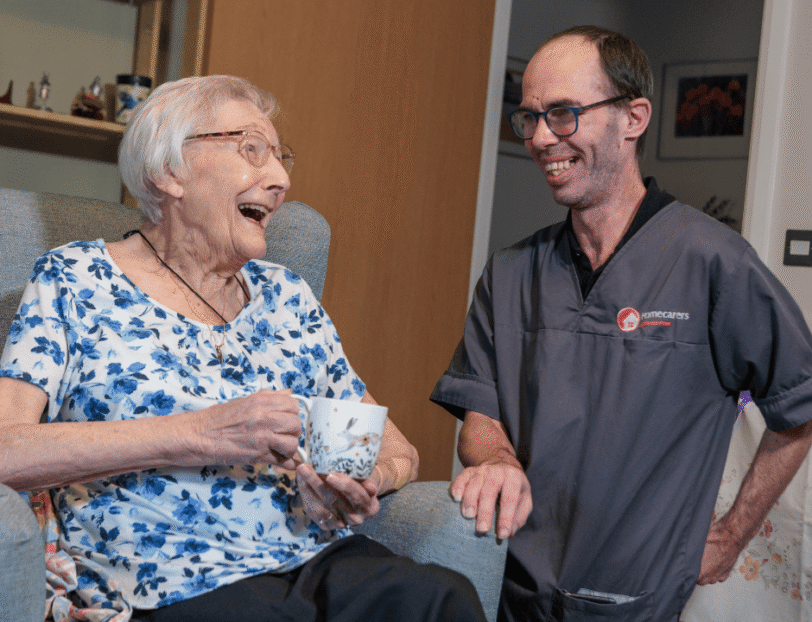 Image of a service user and a Care Assistant, smiling and laughing whilst holding a cup of tea.